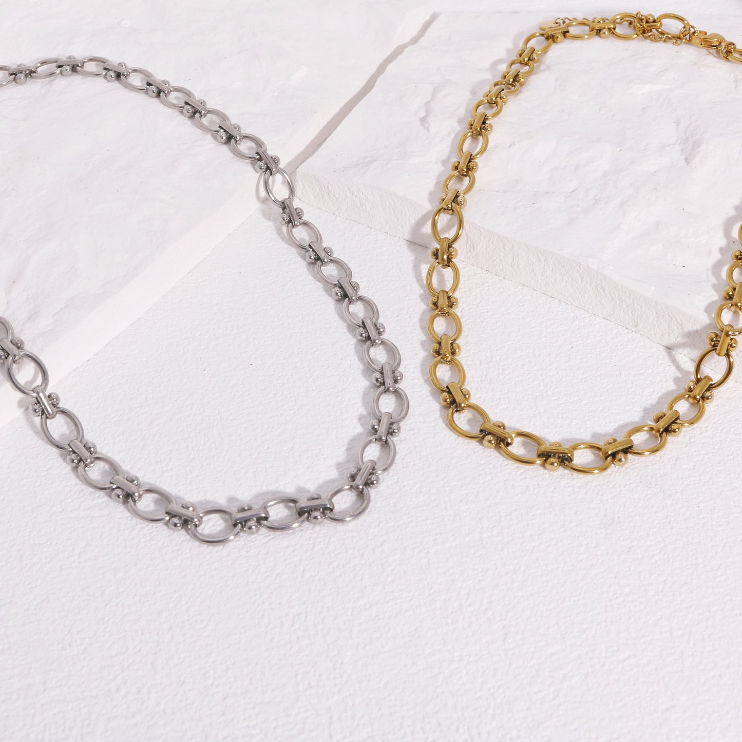 Two stainless steel chain necklaces with oval links, one with a silver finish and the other with a gold finish, displayed on a white surface.