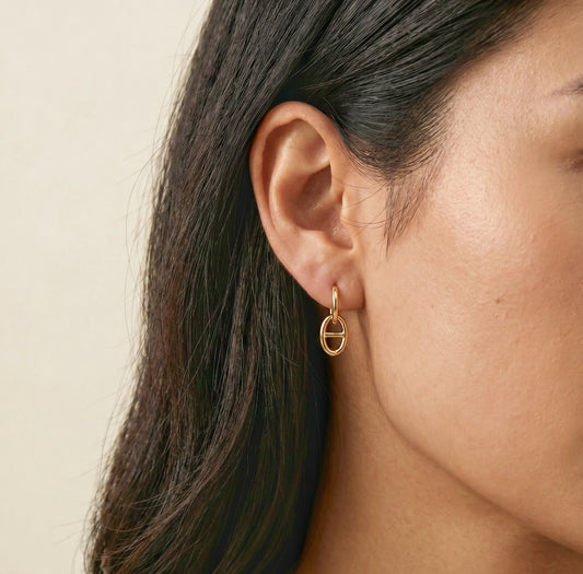 Close-up of a person wearing a gold earring with a beige background
